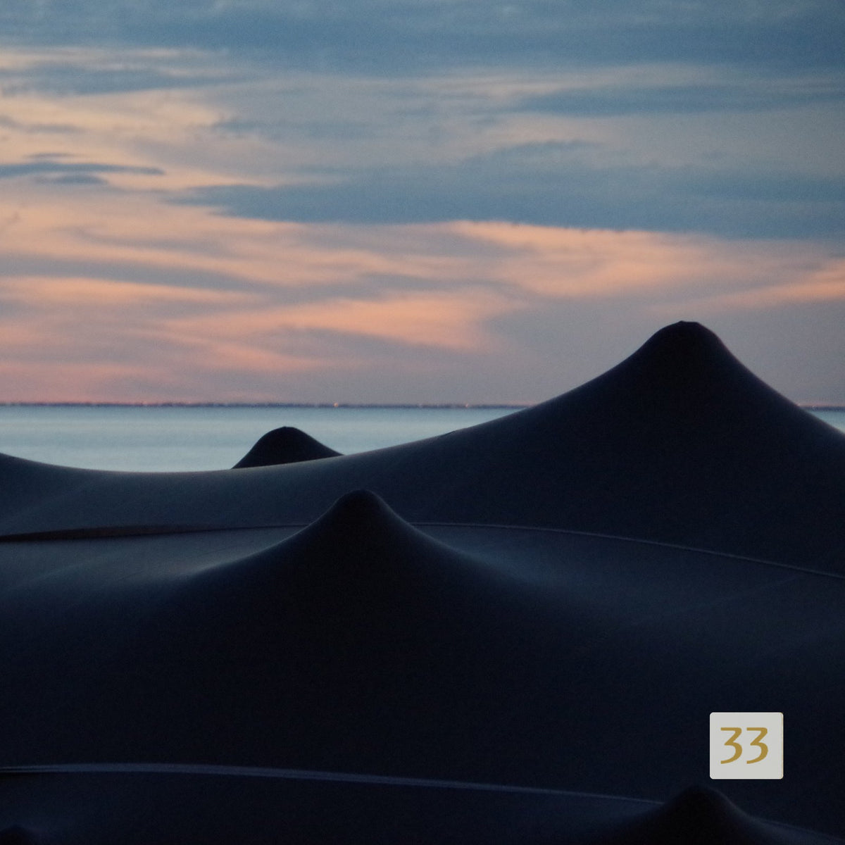 Silhouette of black BT stretch tent peaks against the sea at sunset